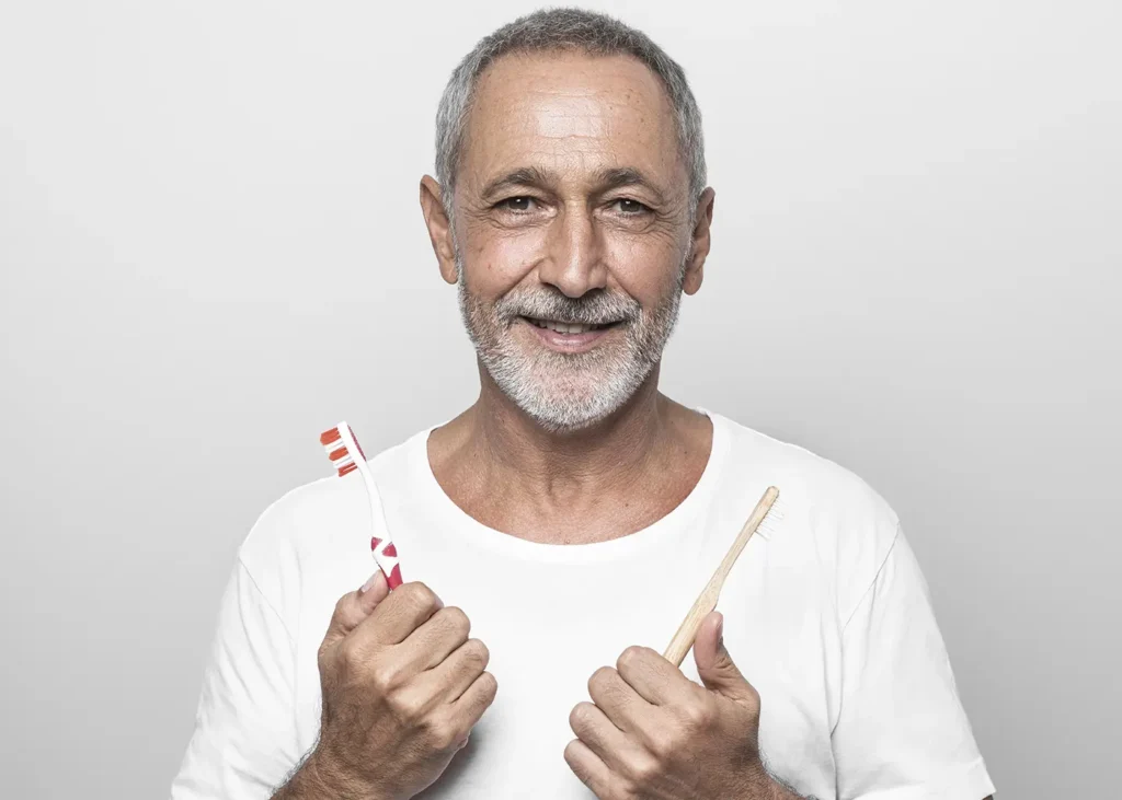 A man smiling and holding toothbrushes, emphasizing the importance of good oral hygiene to prevent teeth problems for individuals with diabetes.