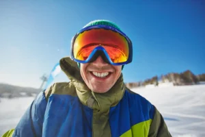 Happy snowboarder in winter gear smiling broadly while enjoying a sunny day on the slopes, demonstrating how to keep your teeth safe during winter activities with tips from Family Dental Group.