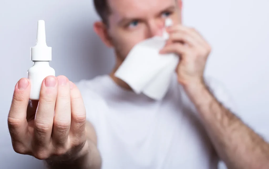 Man using nasal spray to relieve allergy symptoms and maintain oral health, highlighting the connection between allergies and oral care