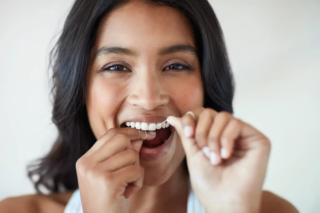 Smiling woman flossing her teeth, highlighting the connection between heart health and oral hygiene practices such as brushing, promoted by Family Dental Group.