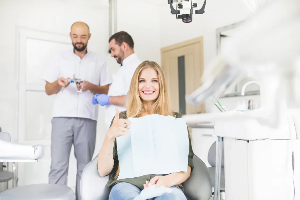 Smiling female patient giving a thumbs-up in a dental chair, with two male dentists in the background, illustrating expert care at Family Dental Group on how to keep your teeth safe.