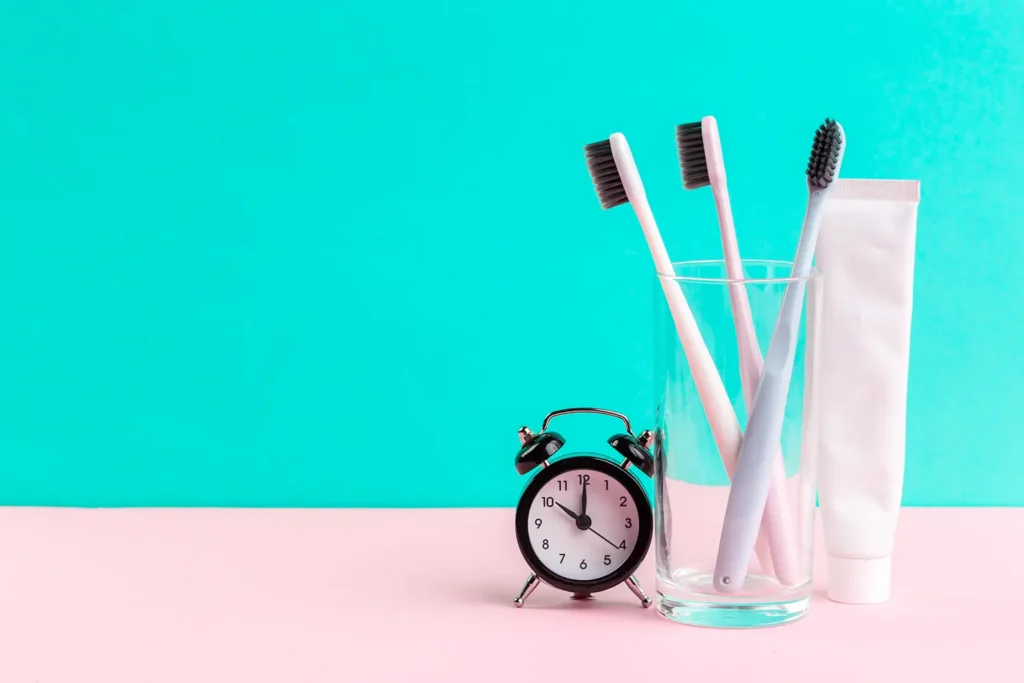 oothbrushes in a glass, toothpaste, and a clock against a bright background, symbolizing good dental hygiene habits recommended by Family Dental Group.