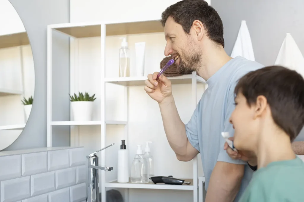 Father and son brushing their teeth together, highlighting the importance of oral hygiene to prevent common dental problems. Family Dental Group emphasizes the role of daily brushing in maintaining healthy teeth and gums.