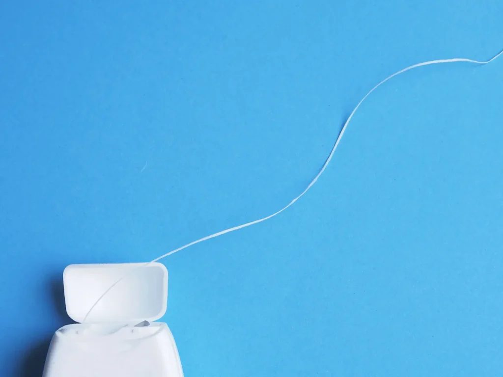 Dental floss container with floss extended against a blue background, illustrating the importance of flossing and addressing concerns about whether flossing can cause receding gums.