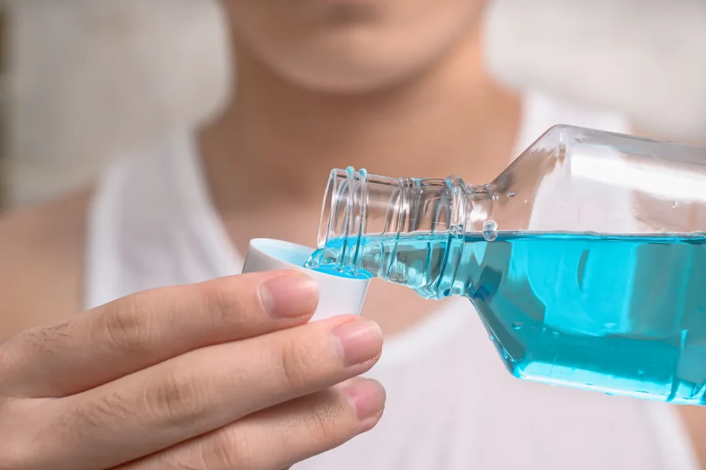 Man pouring mouthwash into a cap, highlighting the importance of oral hygiene for those who struggle to floss between my teeth due to tight teeth.