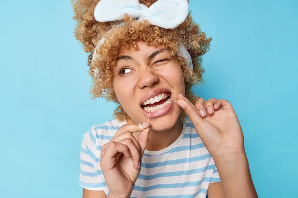 Young woman using dental floss and struggling to floss between my teeth due to tight teeth, emphasizing the challenges of maintaining oral hygiene.